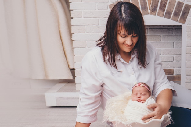 Moeder knuffelt de baby. een pasgeboren baby, gewikkeld in een deken, slaapt in een mand tegen de achtergrond van de open haard. concept van kindertijd, gezondheidszorg, ivf, gezinswoning