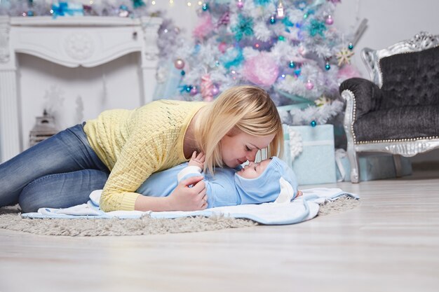 Moeder knuffelt haar baby bij de kerstboom. het concept van Kerstmis