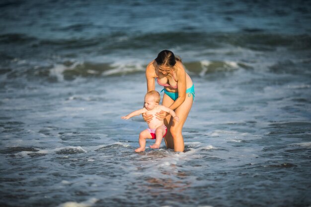 moeder knuffelt haar babyjongen op de oceaangolf Concept van eenheid en tedere verbinding tussen een jonge moeder en zijn lieve kind