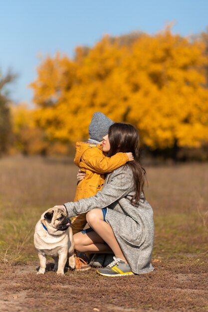 Moeder knuffelt het kind tijdens een herfstwandeling met de hond in het park.