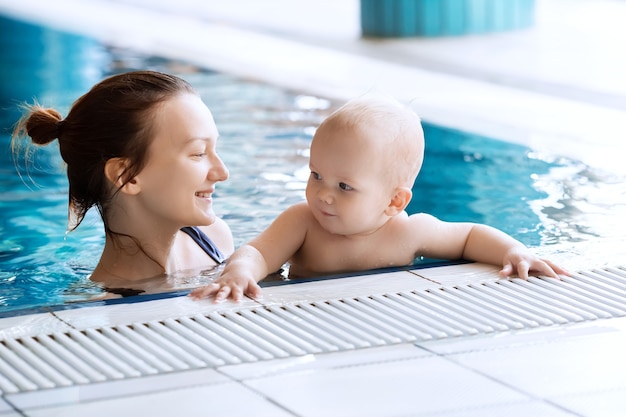 Moeder leert baby zwemmen Portret van een charmant kind van 11 maanden in de klas in een zwembad