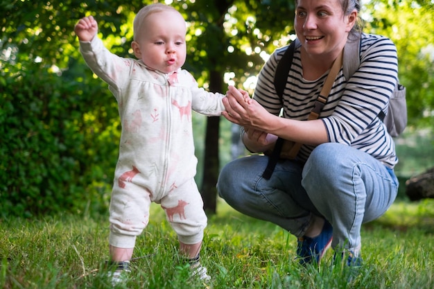 Moeder leert babydochter eerste stappen in het park te lopen op een warme zomerdag