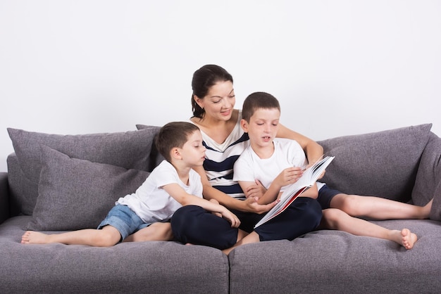 Moeder leest een interessant boek met haar zonen van de sofa Studio portret op witte achtergrond