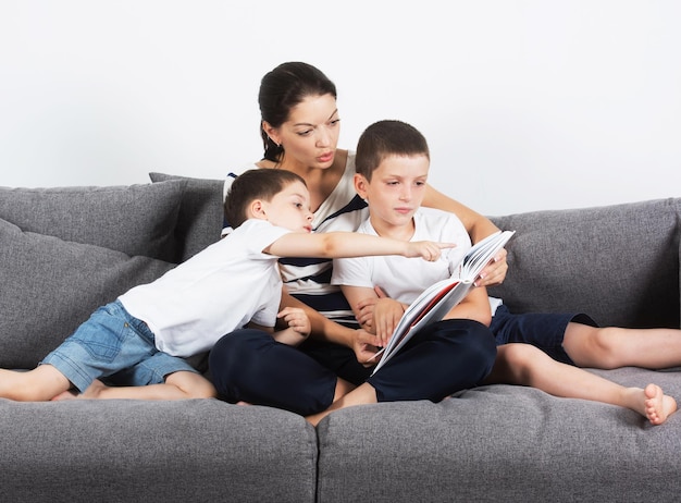 Moeder leest een interessant boek met haar zonen van de sofa Studio portret op witte achtergrond