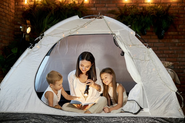 Moeder leest kinderen een verhaaltje voor voor het slapengaan thuis in een tent