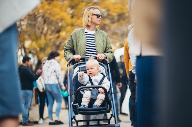 Moeder loopt en duwt zijn baby jongen kind in een kinderwagen in een menigte mensen op een zondag vlooienmarkt in Malaga Spanje