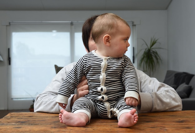 Foto moeder met baby die thuis aan tafel zit en opzij kijkt