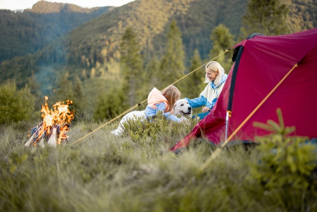 Moeder met dochter en hond zitten bij het kampvuur in de buurt van tent op de natuur