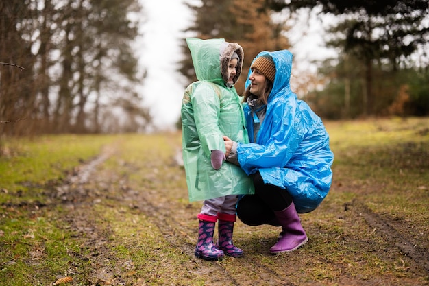 Moeder met dochter in het bos na regen samen in regenjassen