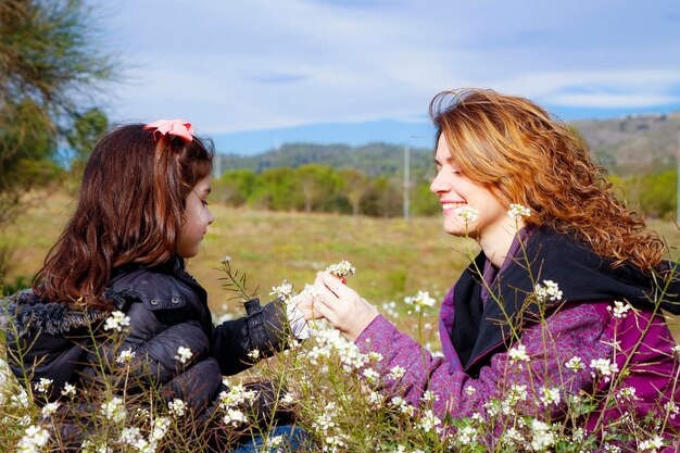 Foto moeder met dochter zit op het grasveld te midden van bloemen tegen de lucht