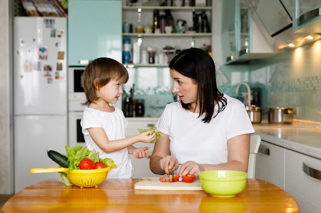 Moeder met dochtertje samen groentesalade maken in de keuken thuis