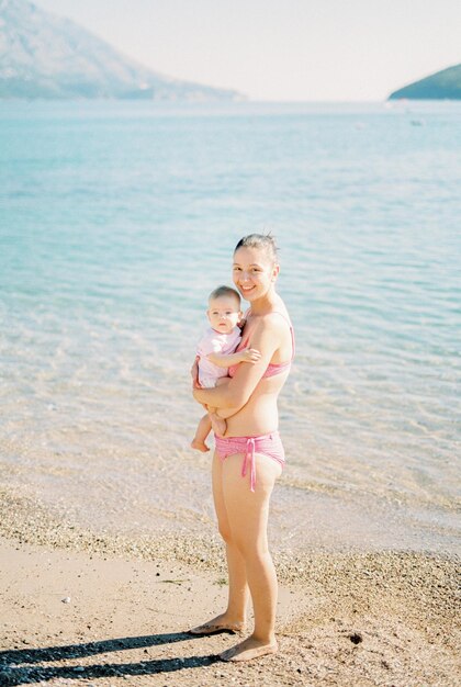 Moeder met een baby in haar armen staat op het strand aan zee