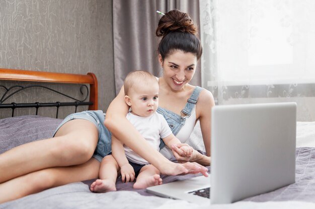 Moeder met een baby werkt vanuit huis op een laptop. Afstandswerk.