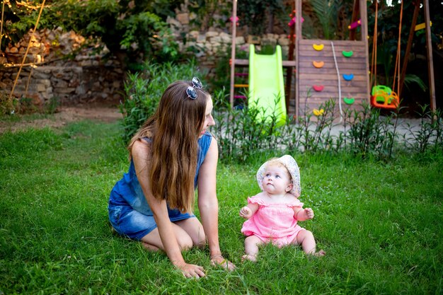 Moeder met een babymeisje op het groene gazon op de speelplaats in de zomer plezier