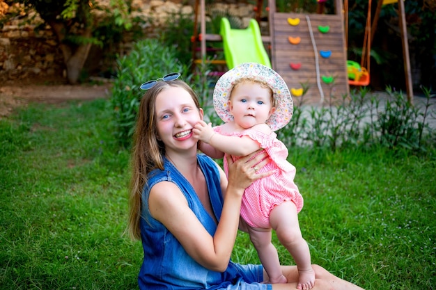 Moeder met een babymeisje op het groene gazon op de speelplaats in de zomer plezier