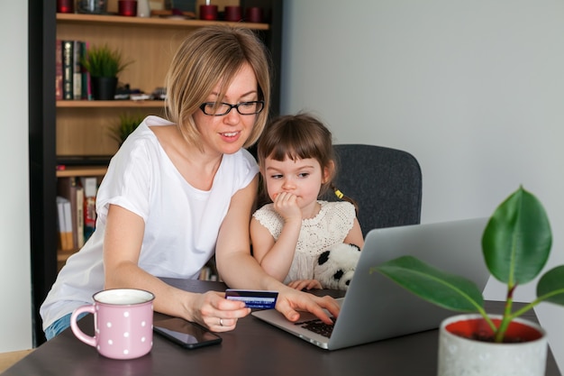 Moeder met een creditcard met haar dochtertje zitten in de buurt van de laptop te kijken. Winkelen online concept.