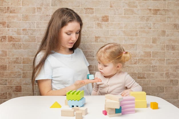 Moeder met een kind dat thuis met houten blokken speelt