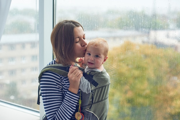 Moeder met ergobaby dragende peuter thuis.