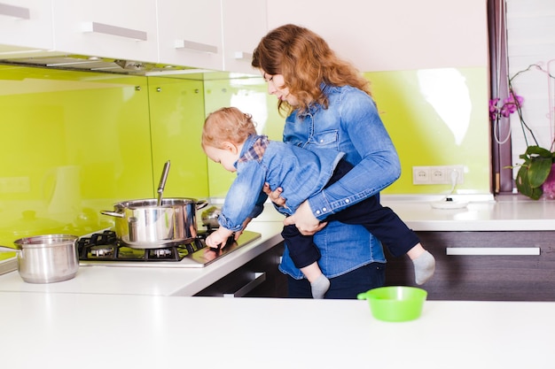 Moeder met haar 1-jarige kind koken in hun keuken. moeder leert babyjongen om gasfornuis te gebruiken. kleine baby. kleine baby zet het gasfornuis uit in de armen van zijn moeder