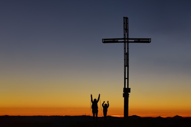 Moeder met kind bovenop de berg bij het kruis heffen hun armen op in overwinning