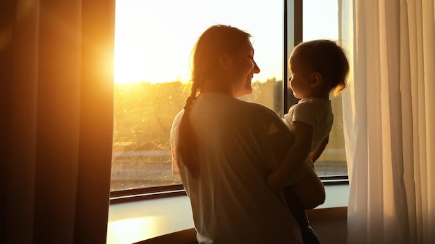Moeder met kind in de armen komt naar het raam en toont zonsondergang