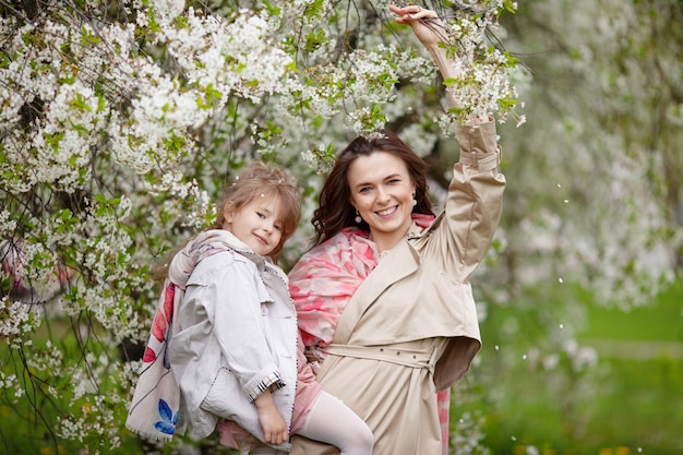 Moeder met kind meisje spelen in bloeiende lentetuin. vrouw met dochter knuffelen en plezier buitenshuis. concept van gelukkige familie