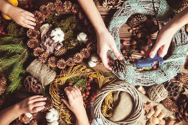 Foto moeder met kinderen die natuurlijke kerstkransen maken om thuis te versieren. bovenaanzicht tafel met handen