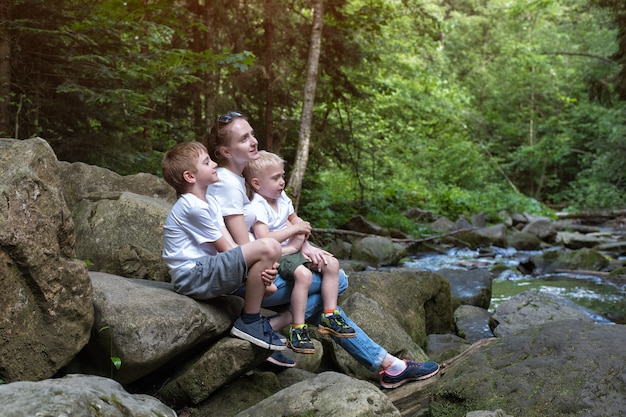 Moeder met kinderen die op een bergrivier en een wild bos zitten. Reis met het gezin. ecotoerisme