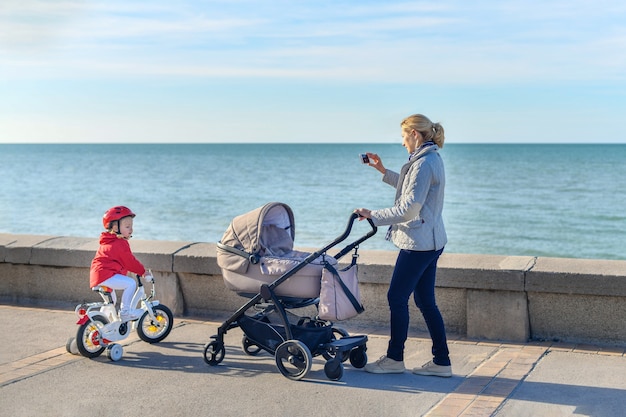 Moeder met kinderwagen en dochter op een fiets lopen samen op het strand