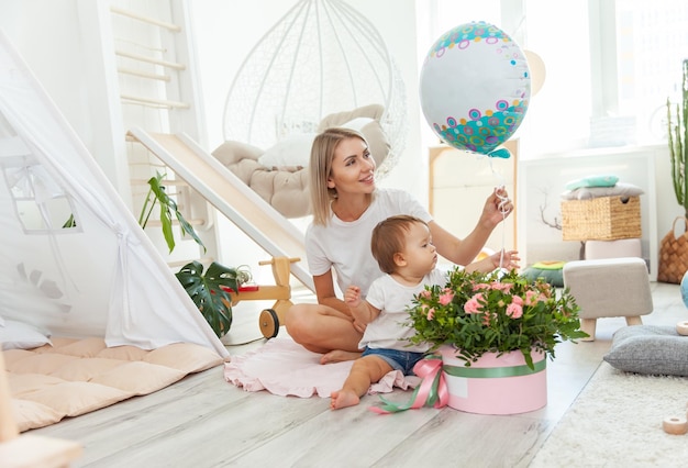 Moeder met kleine baby dochter vieren verjaardag met ballon en boeket rozen thuis