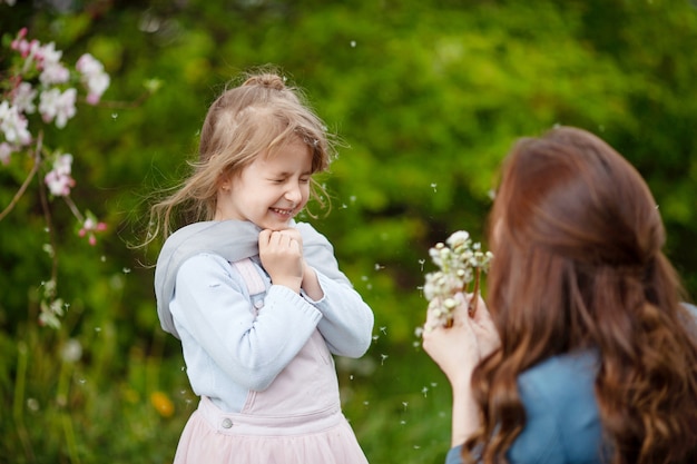 Moeder met kleine dochter waait aan paardebloem - levensstijl buitenshuis scène in park. Gelukkig gezin concept