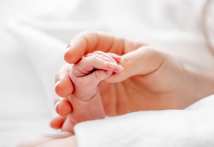 Foto moeder met kleine pasgeboren babyhand met kleine vingers close-up in het bed met wit beddengoed met daglicht. concept van matherinity liefde, bescherming en tederheid