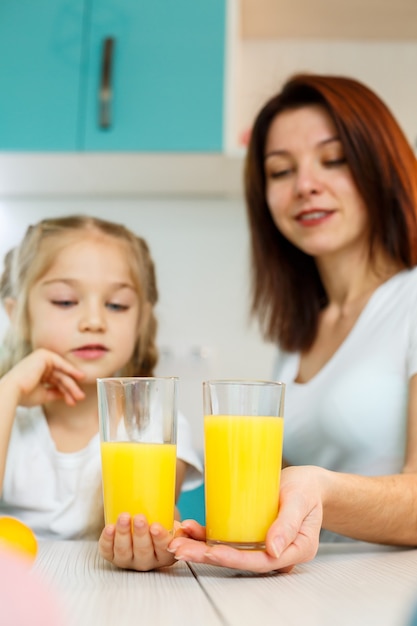 Moeder met meisje dat sinaasappelsap drinkt terwijl ze samen ontbijten