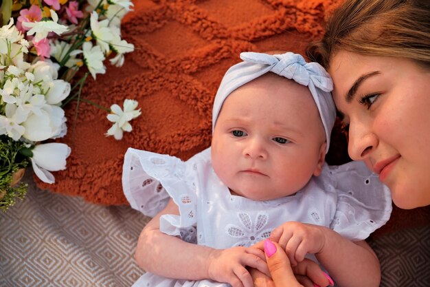 Moeder met pasgeboren baby ligt op het strand witte jurken bloemen liggen vlakbij