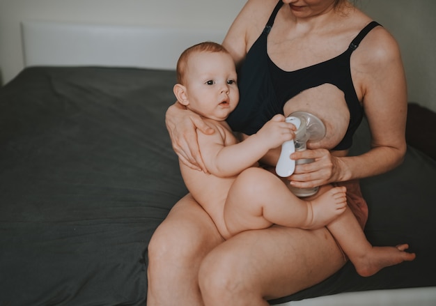 Moeder met pasgeboren babyjongen die hem in haar armen houdt terwijl ze de borstkolf knuffelt