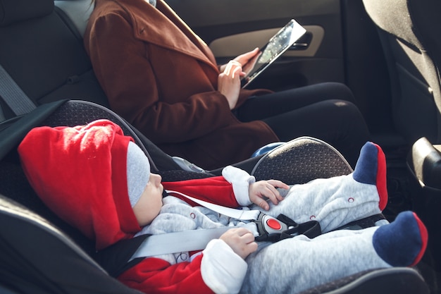 Moeder met tablet in haar handen en haar zoontje in een baby-autozitje rijden op de achterbank van een taxi