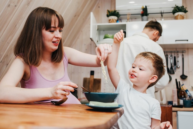 Moeder met vader die het kind in de keuken voedt met pasta