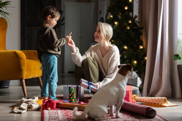 Moeder met zoon verpakken kerstcadeaus thuis op een vloer.