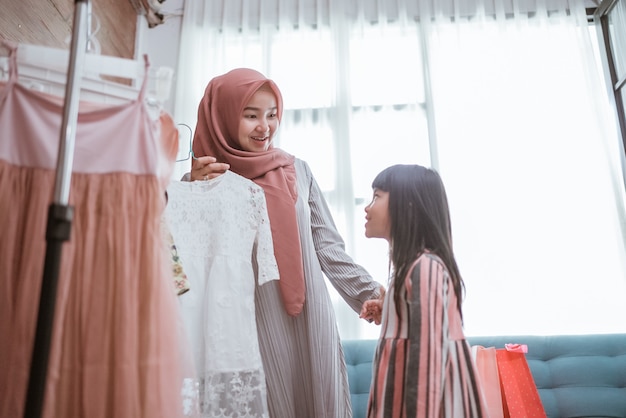 Moeder moslim die samen een jurk kiest voor haar dochter in een kledingwinkel. moeder en kind winkelen in boetiek