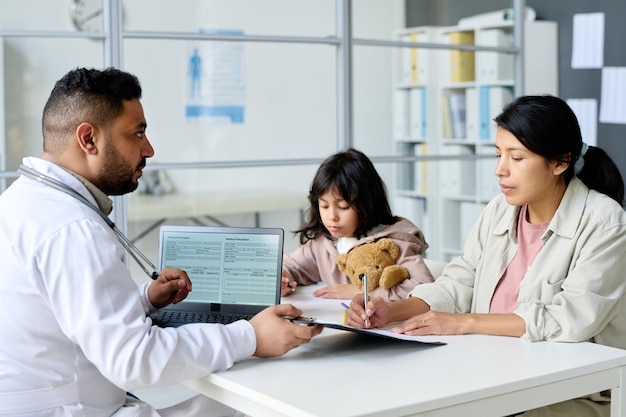 Moeder ondertekent document voor vaccinatie van haar kind tijdens hun bezoek aan het ziekenhuis