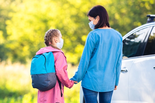 Moeder ontmoet dochter na school tijdens pandemie naast auto op zonnige dag