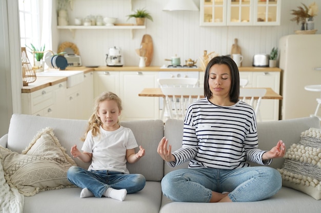 Moeder pleegdochter beoefent yoga zittend op de bank thuis gezonde levensstijl adoptie van kind