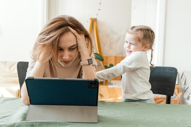 Moeder probeert met haar dochter thuis te werken op een tablet Quarantaine en werken op afstand tijdens de uitbraak van het coronavirus Het kind maakt lawaai en stoort de vrouw op het werk vanuit huis