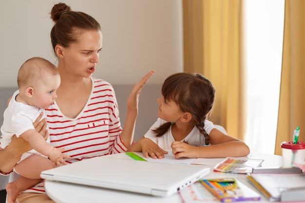 Moeder raakt gefrustreerd door dochter terwijl ze huiswerk maakt terwijl ze thuis aan tafel zit met leerproblemen, huiswerk, ouderschap en online onderwijs.