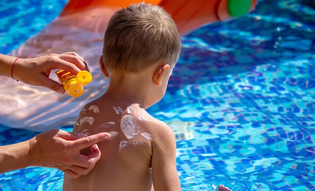 Moeder smeert crème op de rug van haar zoon Zorgen voor babyhuid Zonnebrandmiddelen in de selectieve focus voor reizen