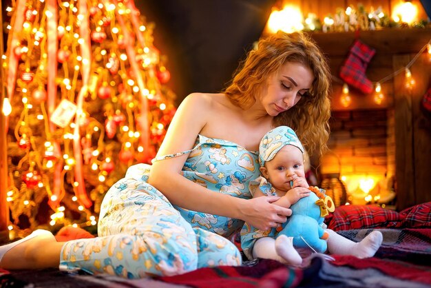 Moeder speelt met baby zittend in de buurt van kerstboom en open haard in ingerichte woonkamer