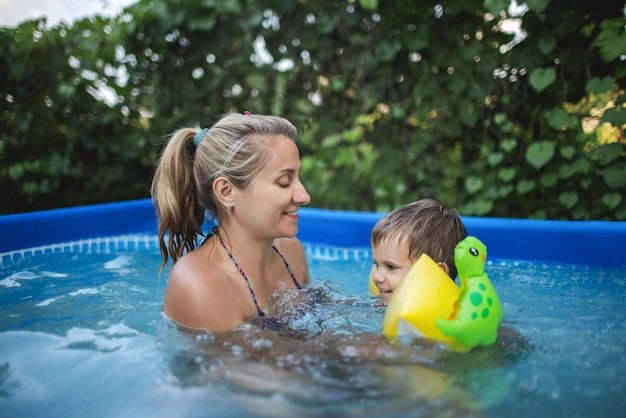 Moeder speelt met een naakte baby in overmouwen in het zwembad tegen de achtergrond van een zomerse zonsondergang