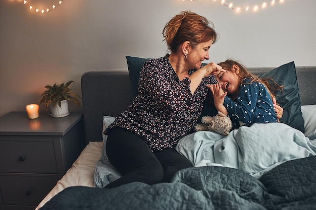 Moeder speelt met haar kleine dochter in bed en heeft plezier voordat ze gaat slapen. Moeder kietelt dochter.