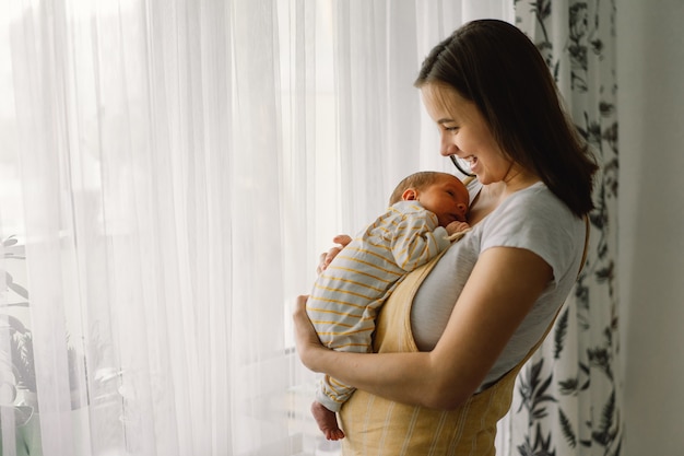 Moeder speelt met pasgeboren zoontje thuis in de buurt van het raam. Gelukkige baby en moeder.