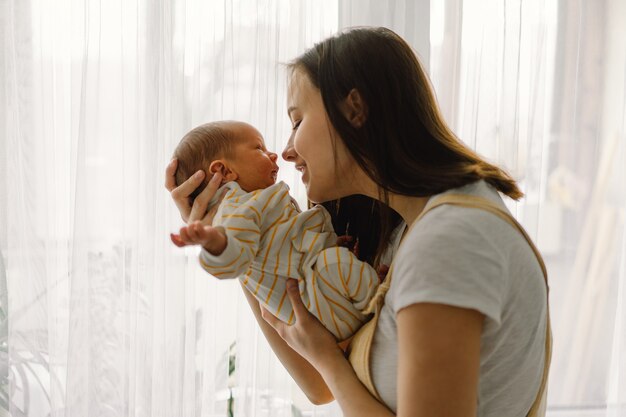 Moeder speelt met pasgeboren zoontje thuis in de buurt van het raam. Gelukkige baby en moeder.